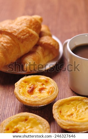 delicious chinese egg tart with croissants, cup of black coffee on wooden background