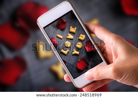 using mobile phone to take photos of Cookies ABC in the form of word I LOVE YOU alphabet  with red rose petal on old jean background, Valentines day