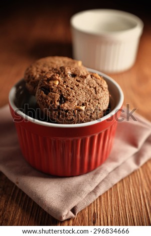 Chocolate cookies on red bowl and pink napkin on wooden background. Chocolate chip cookies shot on colored cloth, closeup.