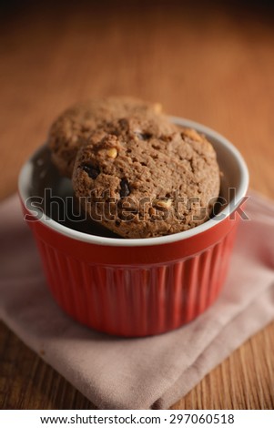 Chocolate cookies on red bowl and pink napkin on wooden background. Chocolate chip cookies shot on colored cloth, closeup.