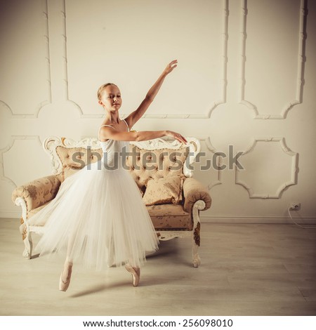 young ballerina is dancing in white hall. She in classic dress is clothed.