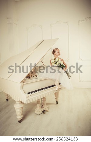 Girl is siting on the white piano. The roses are lie on the piano keys