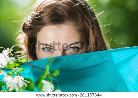 young woman\'s face covered with a blue handkerchief. We can see her eyes green. In her hand she holds a sprig of flowering apple tree.