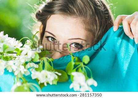 young woman\'s face covered with a blue handkerchief. We can see her eyes green. In her hand she holds a sprig of flowering apple tree.