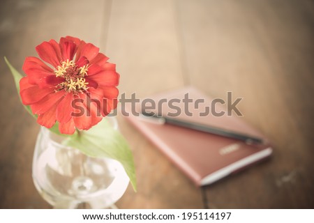 red flower in vase on desk and blown book