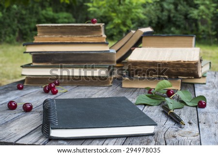 black notebook on wooden table in the garden with old books stacked on background