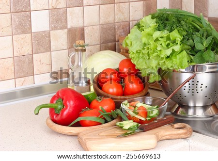The fresh washed-up vegetables in a colander and the cut vegetables on a chopping board against modern kitchen.