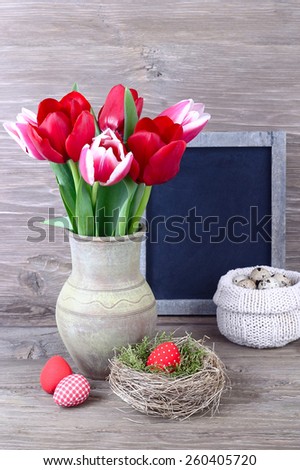 Tulips in a clay vase, a blackboard (a cretaceous board) and Easter eggs in a nest on wooden a rustic a background. An easter background with a place for the text.