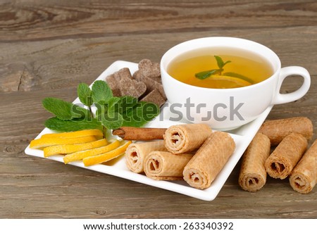 Cup of green tea, lemon, mint, cinnamon and wafers on a white square plate on a wooden background.