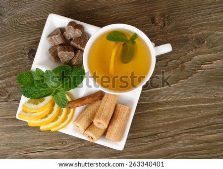Cup of green tea, lemon, mint, cinnamon and wafers on a white square plate on a wooden background. Top view.