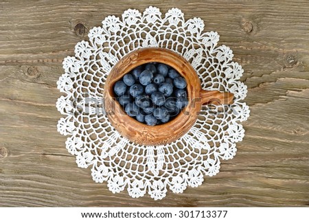 Fresh blueberry in a clay small jug on a lacy napkin on a wooden background. Top view.