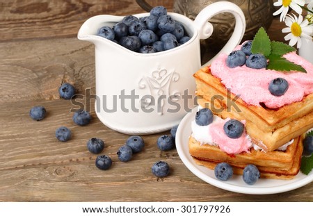 Fresh biscuits with bilberry mousse and blueberry and milk in a transparent jug on a wooden background.