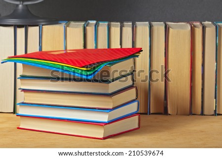 Pile of books on a wooden surface against the background of a number of books.