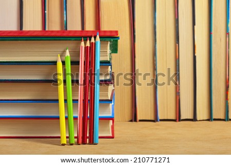Pile of books and colored pencils on a wooden surface against the background of a number of books.