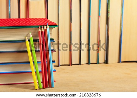 Pile of books and colored pencils on a wooden surface against the background of a number of books.