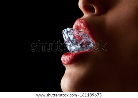 Ice cube in a woman\'s mouth against black background.