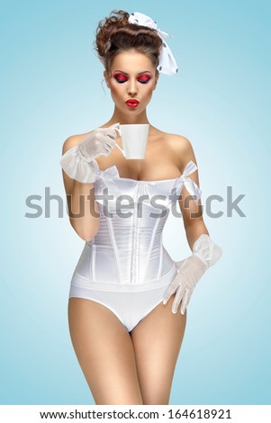 The retro photo of a vintage pin-up girl drinking a morning cup of tea, wearing a corset and stylish makeup.