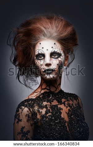 A girl posing in a creepy halloween costume of a witch with peircing and cracked painted face.
