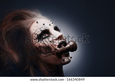 A Creative Photo Of A Queens Painted Pierced Face Holding A Chess King In Her Mouth.