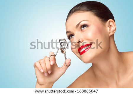 A beautiful fashion girl holding an eyelash curler in her hand as a makeup accessory.