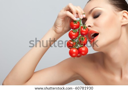 Woman with tomatoes. Side portrait of open mouthed young woman with red tomatoes on vine, studio background.