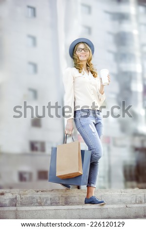 Happy young trendy woman drinking take away coffee and walking down the stairs after shopping with bags in an urban city.