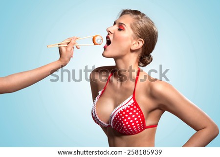 A creative retro photo of a young pin-up girl in bikini eating sushi from chopsticks.