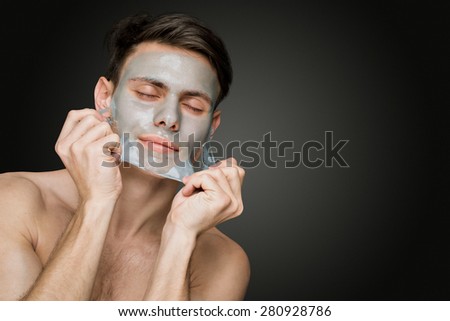 Portrait of a beautiful young man peeling off a facial mask, face and body skin care retreat.
