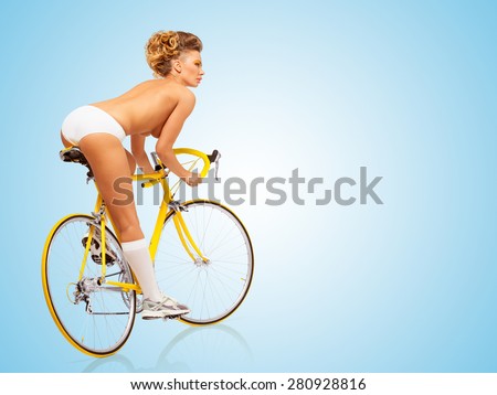 Retro photo of a nude sexy pin-up girl in white erotic panties riding a yellow racing bicycle on blue background.