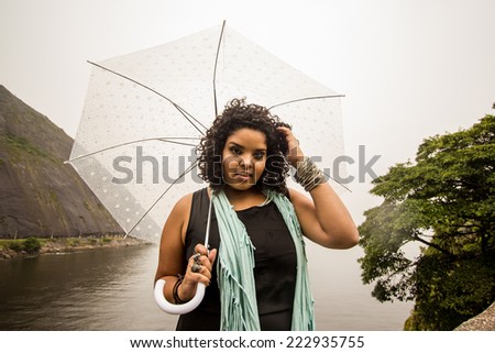 Brazilian model posing in the rain while holding a translucent umbrella