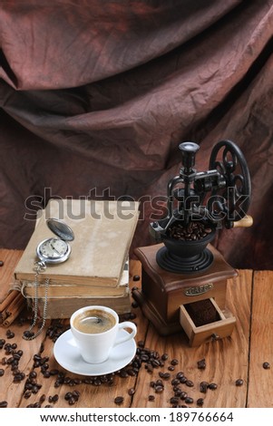 cup of coffee, coffee grinder, coffee beans, antique clocks, old books on a wooden board