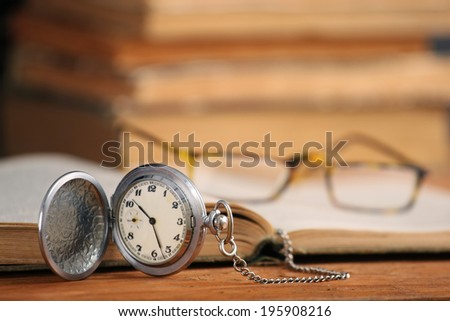 Vintage pocket watch glasses  and open old book on background of wooden planks