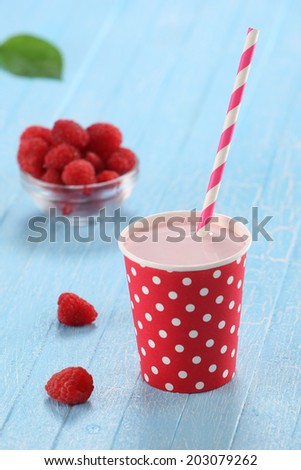 raspberry yogurt cup with a straw on a background of blue painted boards