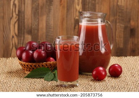 plum juice in a glass and pitcher, plums in a wicker basket on a mat and boards