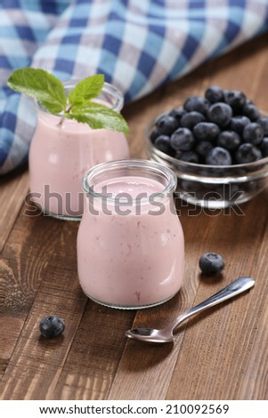 yogurt with blueberries in a glass jar and blueberries in a glass bowl on the background of wooden boards