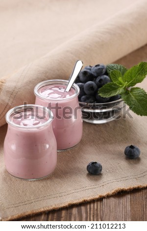 yogurt with blueberries in a glass jar and blueberries in a glass bowl on a wooden boards background and cotton napkins
