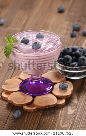 yogurt with blueberries in a glass bowl and blueberries in a glass bowl on the background of wooden boards