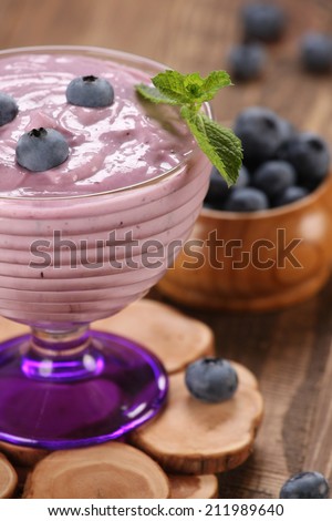 yogurt with blueberries in a glass bowl and blueberries in a glass bowl on the background of wooden boards