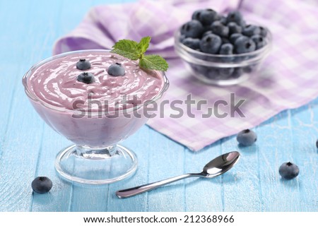 yogurt with blueberries in a glass bowl and blueberries in a glass bowl on a wooden background painted boards