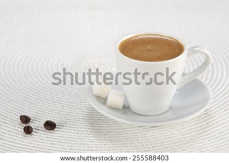 cup of coffee, sugar cubes, coffee beans on a white wicker a mat