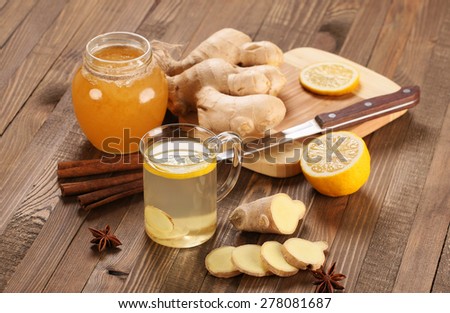 ginger tea in a cup of glass, ginger, lemon, cinnamon, star anise, honey on the background of wooden boards