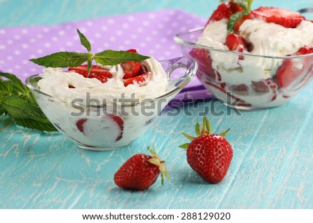 strawberries with cream in a bowl of glass on the background of painted boards