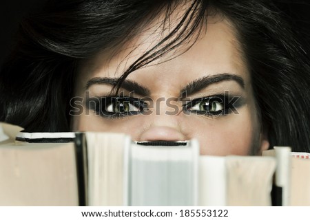 Angry stressed girl student hiding behind a book shelf
