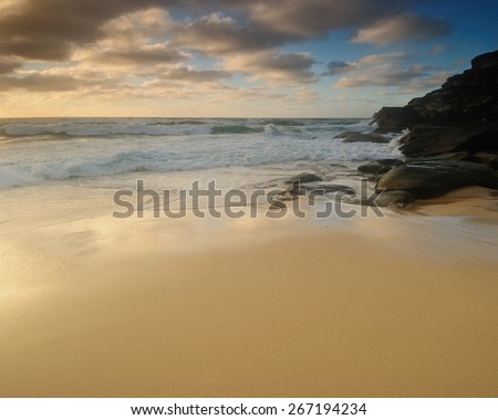Sand beach with soft and smooth water and clouds and some rocks and with wide sand line