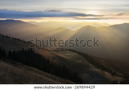Mountain landscape with Sun behind the clouds producing warm and positive sun rays