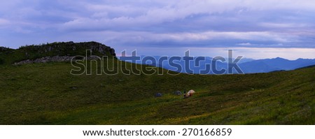 Night mountains landscape with yellow flower meadow hills and slopes and base camp and cloudy sky