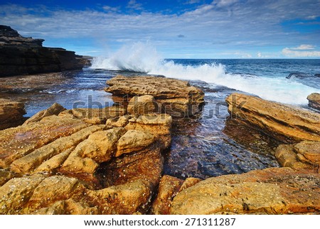 Day seascape with rocky platform and crashing waves in distance and with some cliffs