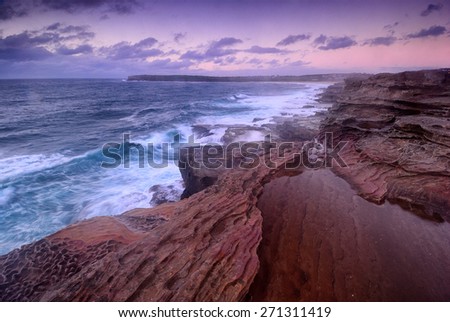 Purple sunrise from the cliff overlooking ocean and distant cliffs and beaches