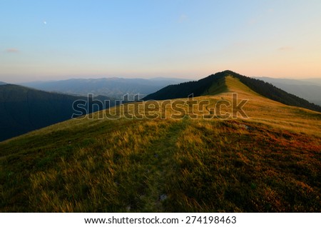 Mountain trail winding through the grass hills with brown grass and soft clouds