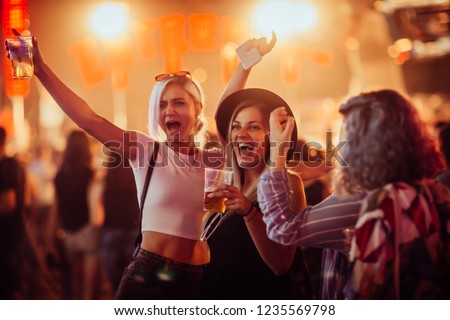Female friends drinking beer and having fun at music festival